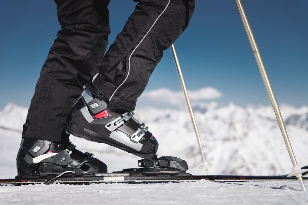 A closup of a person wearing ski shoes skiing in snow