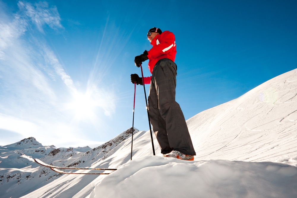 A view of a man standing at a snowy slope holding ski sticks