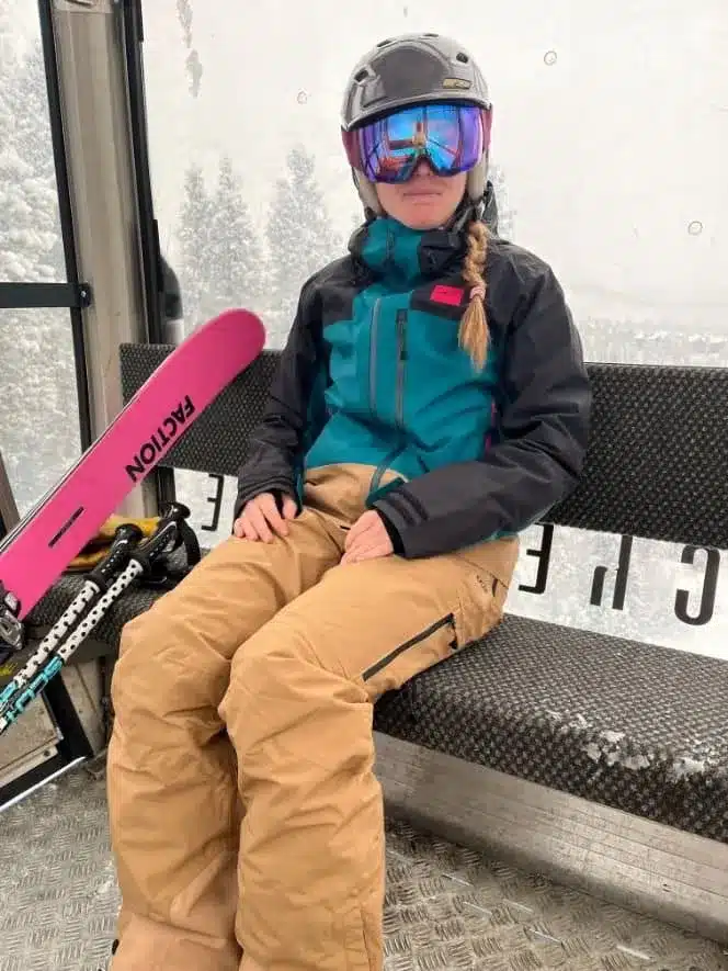 a girl sitting on a bench wearing ski gear