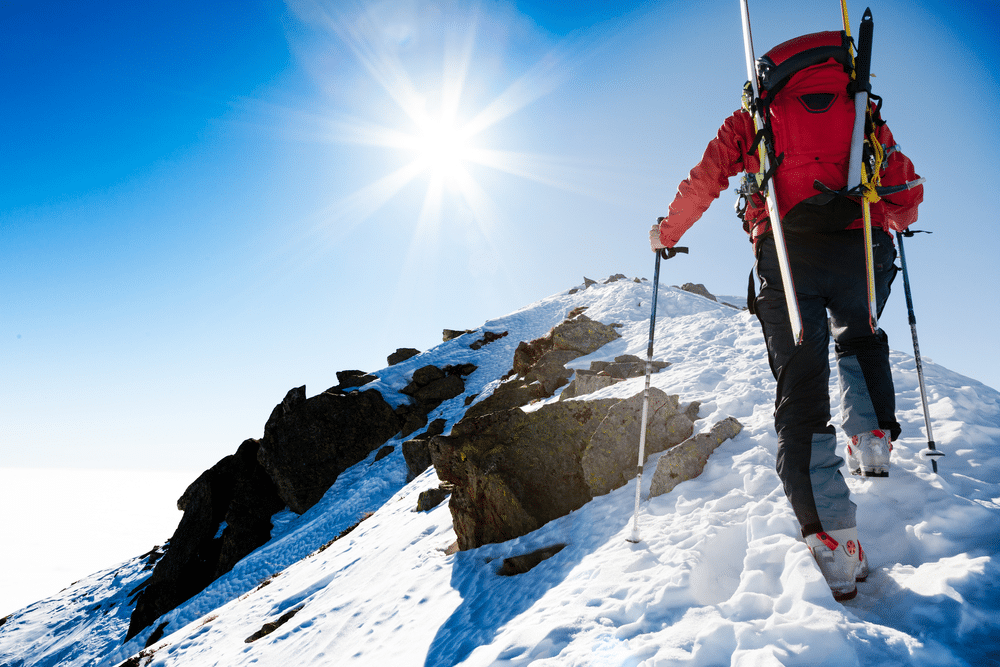 Mountaineer walking up along a snowy ridge with the skis in the backpack