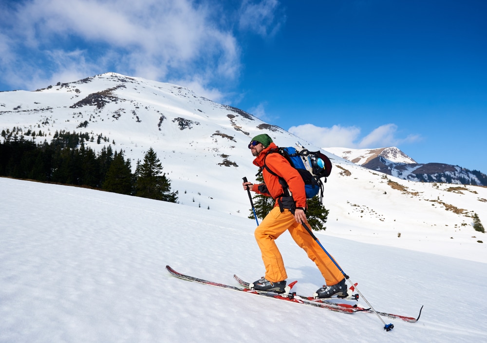 Skier tourist backpacker happy bearded man hiking on skis up hill