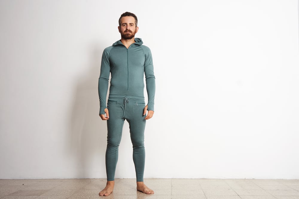 Young fitted bearded male wears thermal base layer suite standing in front of white wall