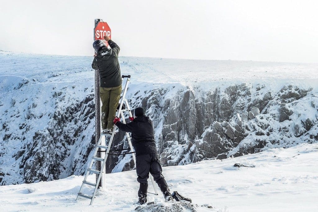 A view of two people using a ladder for putting saftey signs in snow A view of two people using a ladder for putting saftey signs in snow