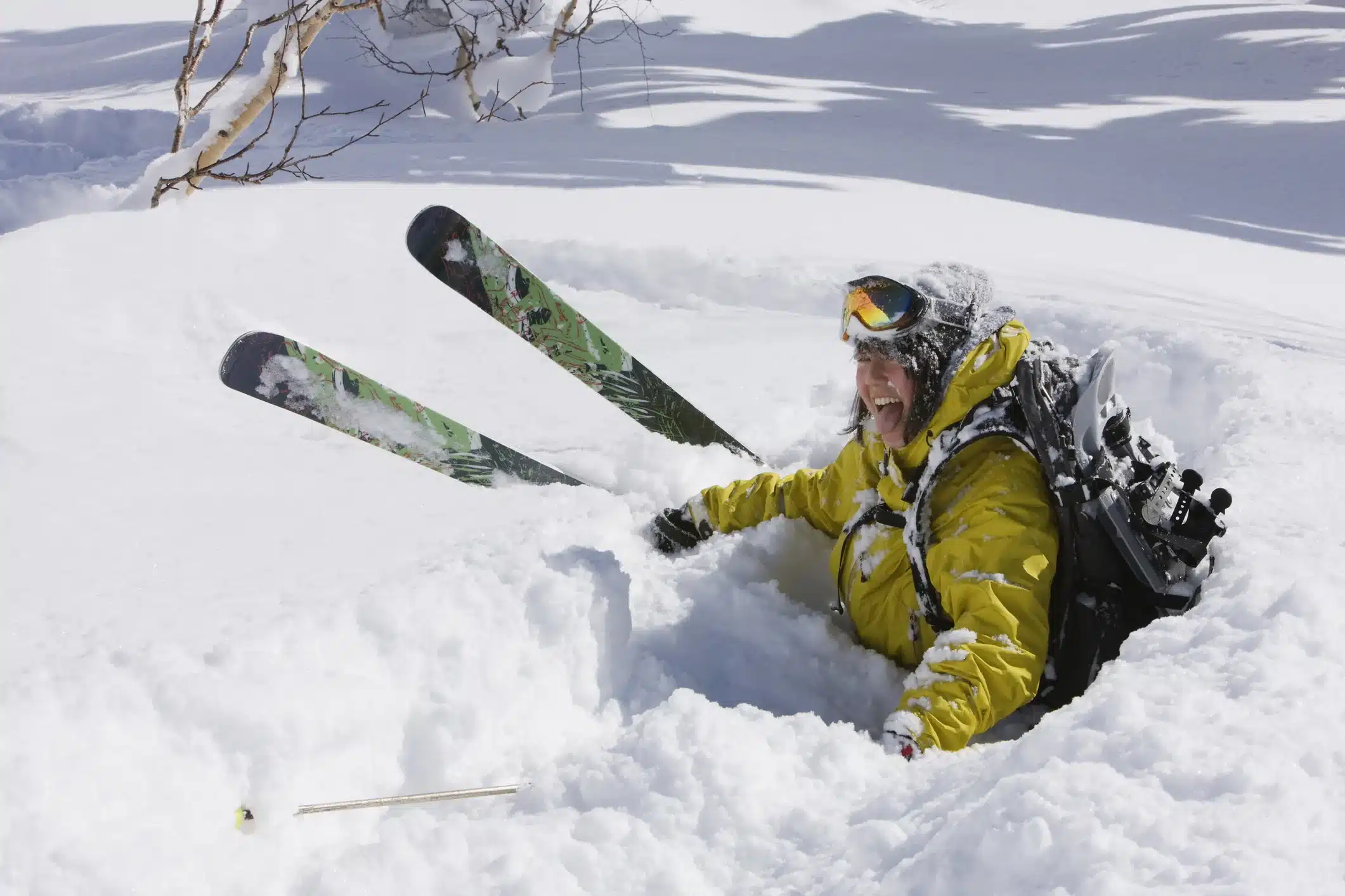 A skier in a bright yellow jacket stuck in deep snow with only their torso visible and skis poking out of the snow