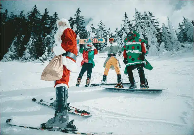 People in holiday costumes including Santa and a Christmas tree skiing and snowboarding on a snowy slope