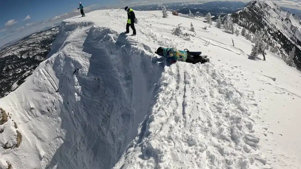 Skiers at the edge of a snowy cliff one skier is kneeling near the edge while others are standing on the slope in the background